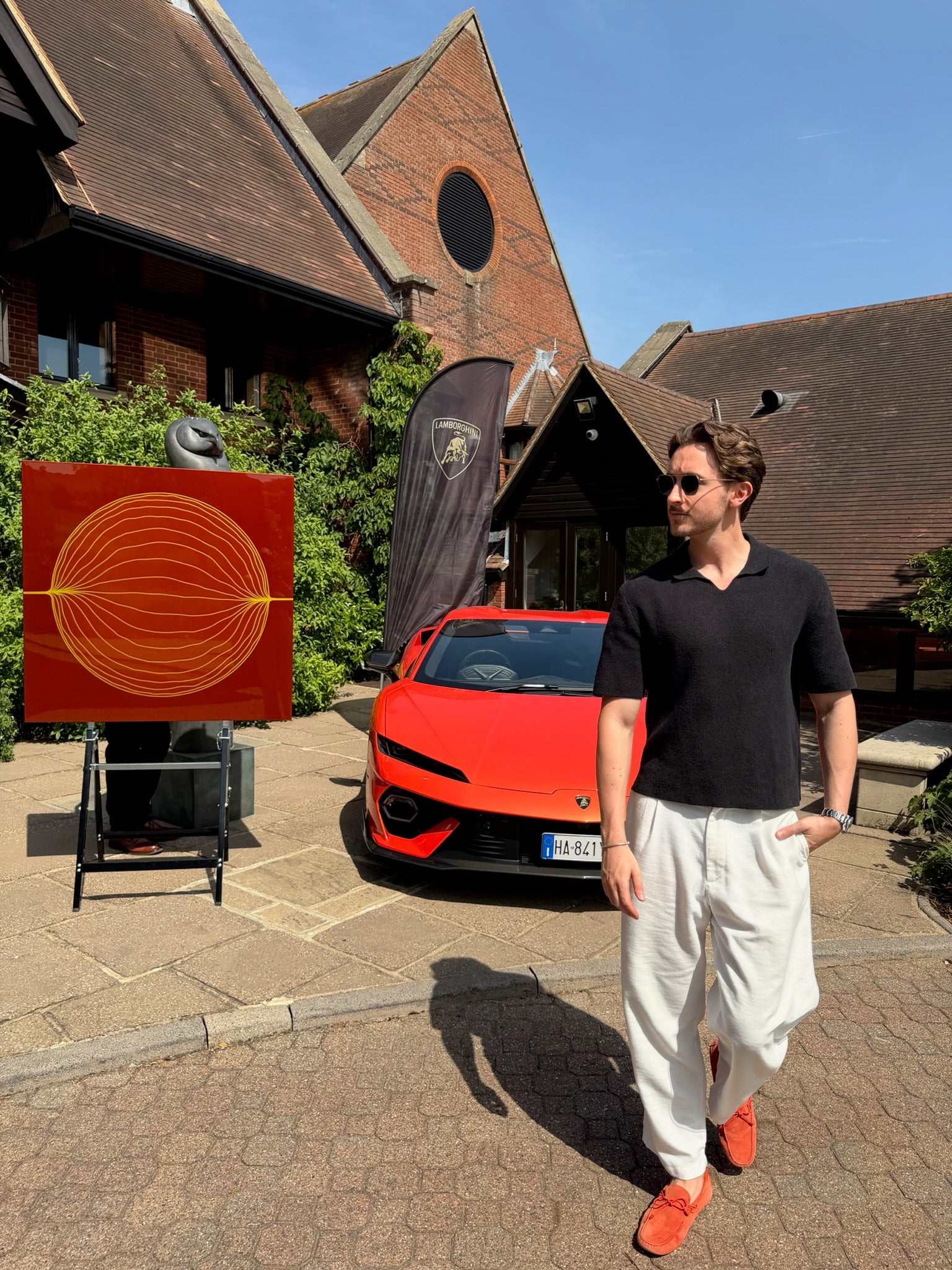 Man standing next to a orange lamboughini temerario at london golf course with artwork by artist russell hatton. 