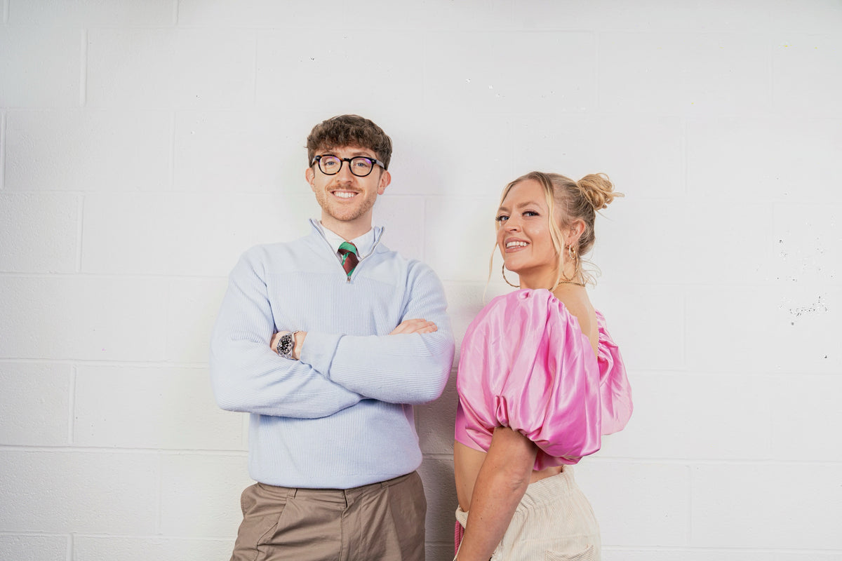 Bella and Ollie, Brother and Sister Art Dealer Duo, specialising in contemporary and abstract art, standing together with a white background wearing pink and blue.