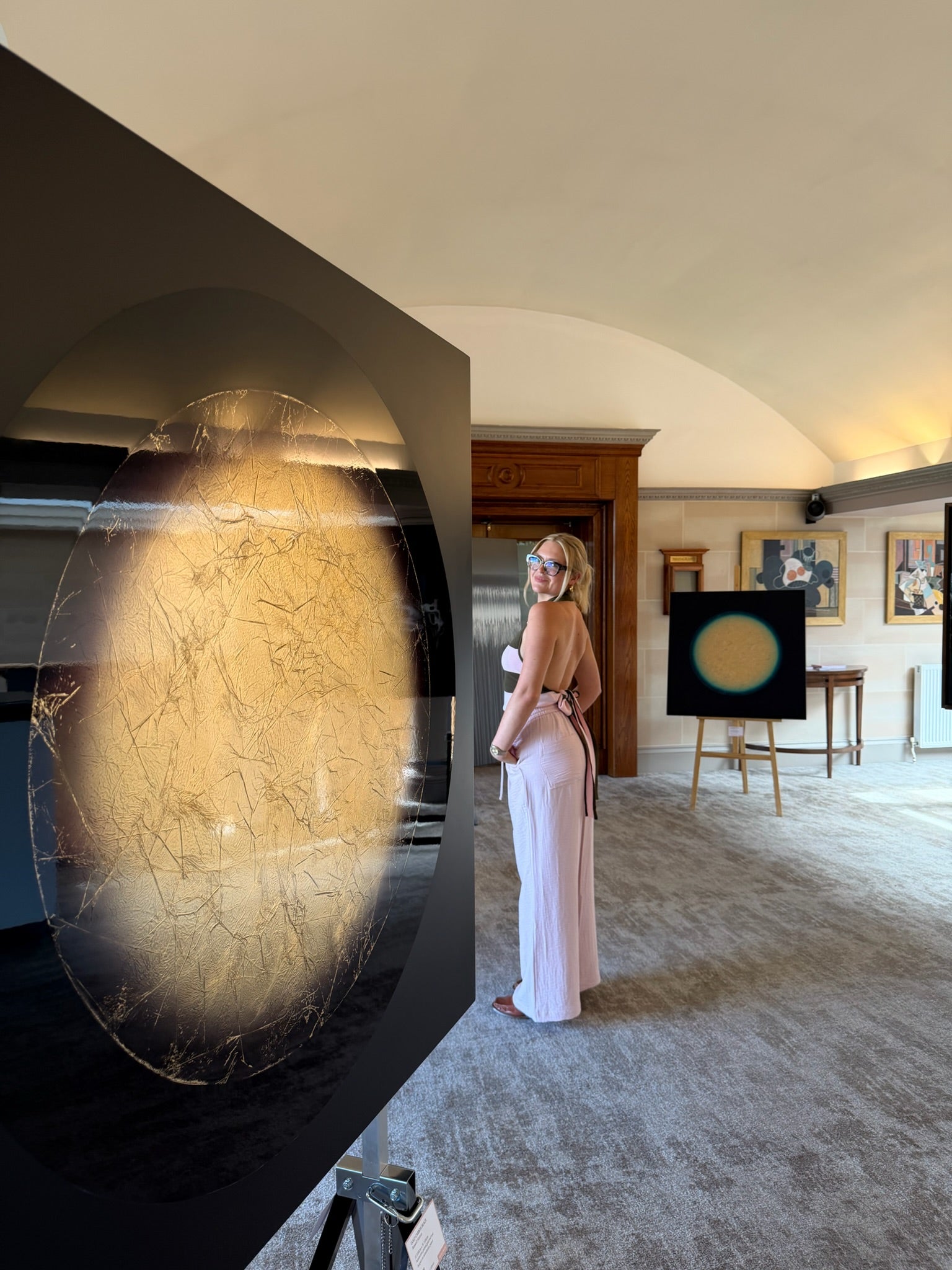 Woman standing in a room with large circular object and Russell hattons rtworks on the wall.