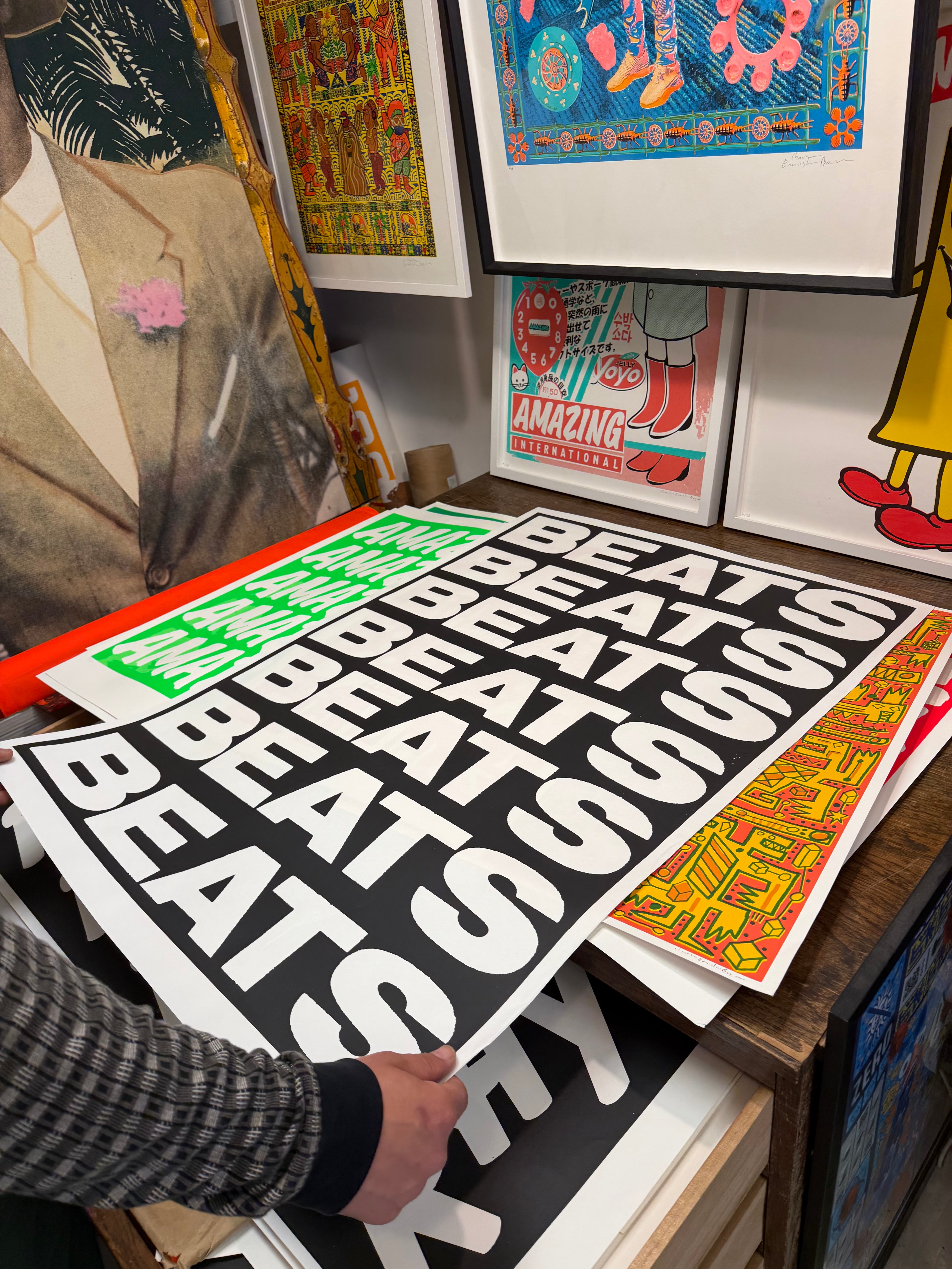 Artist charlie evaristo boyce  holding a 'BEATS' poster among various framed artworks on a studio table.