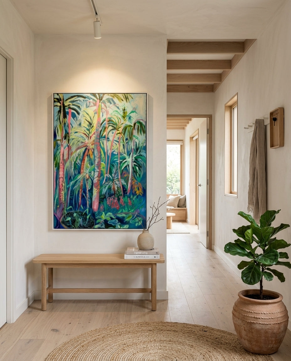 A large framed painting of a tropical barbados palm forest hangs on a white wall in a bright, modern scandinavian hallway with light wood floors, a wooden bench, and a potted plant. contemporary artwork for your home by artist Hannah Rollings. 
