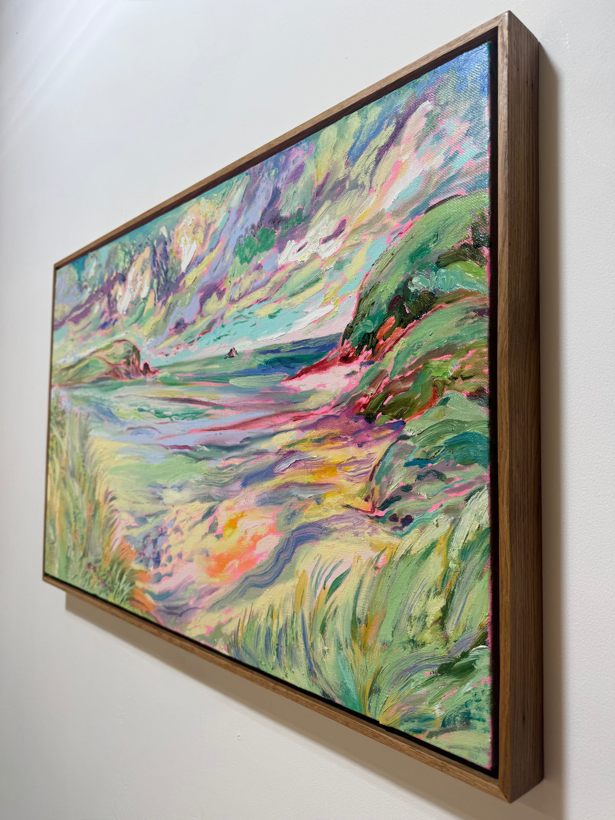 A framed landscape painting with vibrant green, blue, pink, and yellow brushstrokes. Across the Shallows 2026 by Hannah Rollings, original colourful landscape painting inspired by Cornwall